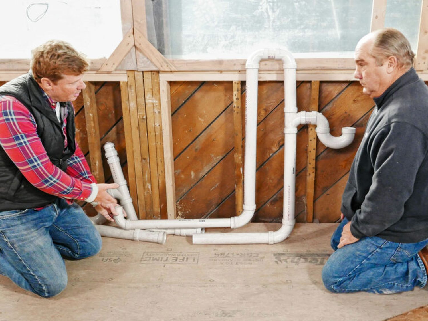 Kevin O'Connor and Richard Trethewey look at PVC pipes that are part of a plumbing project.